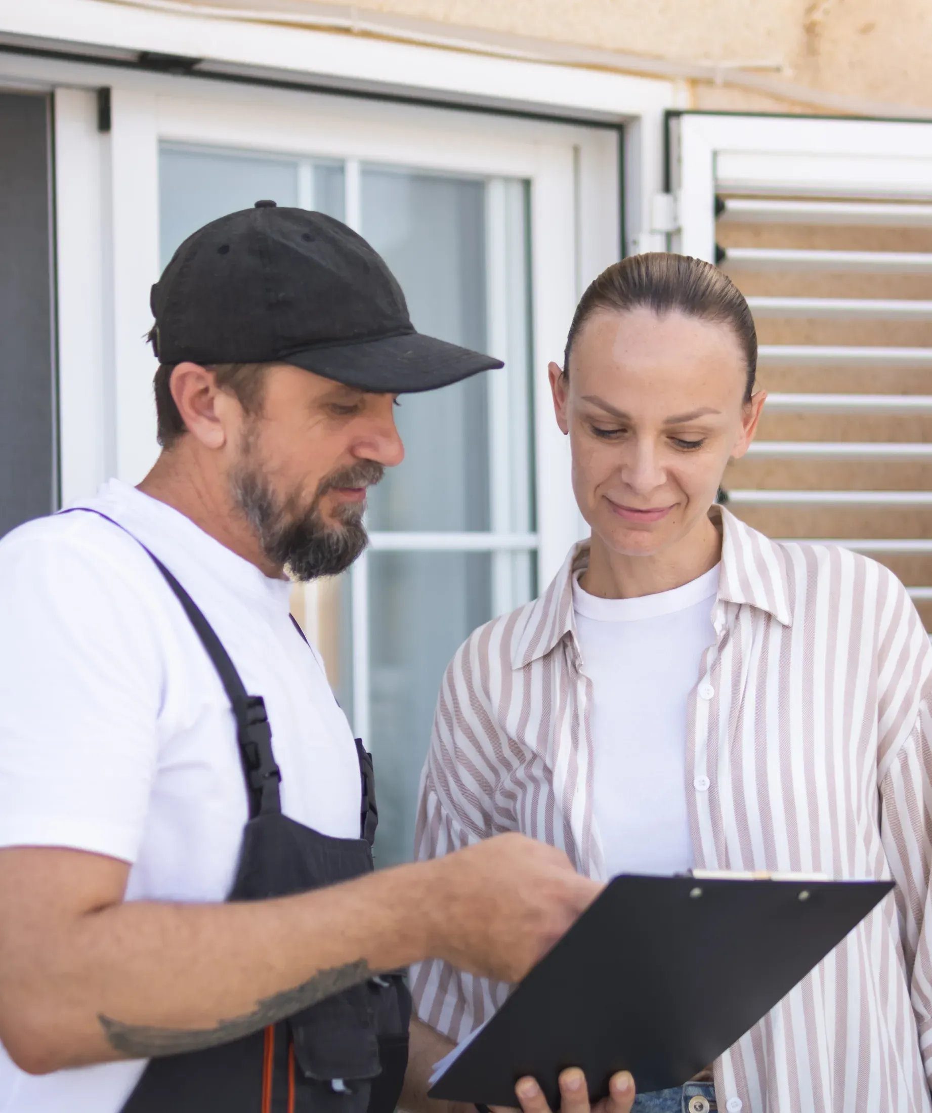 A contractor and a homeowner reviewing paperwork on a clipboard outside a house