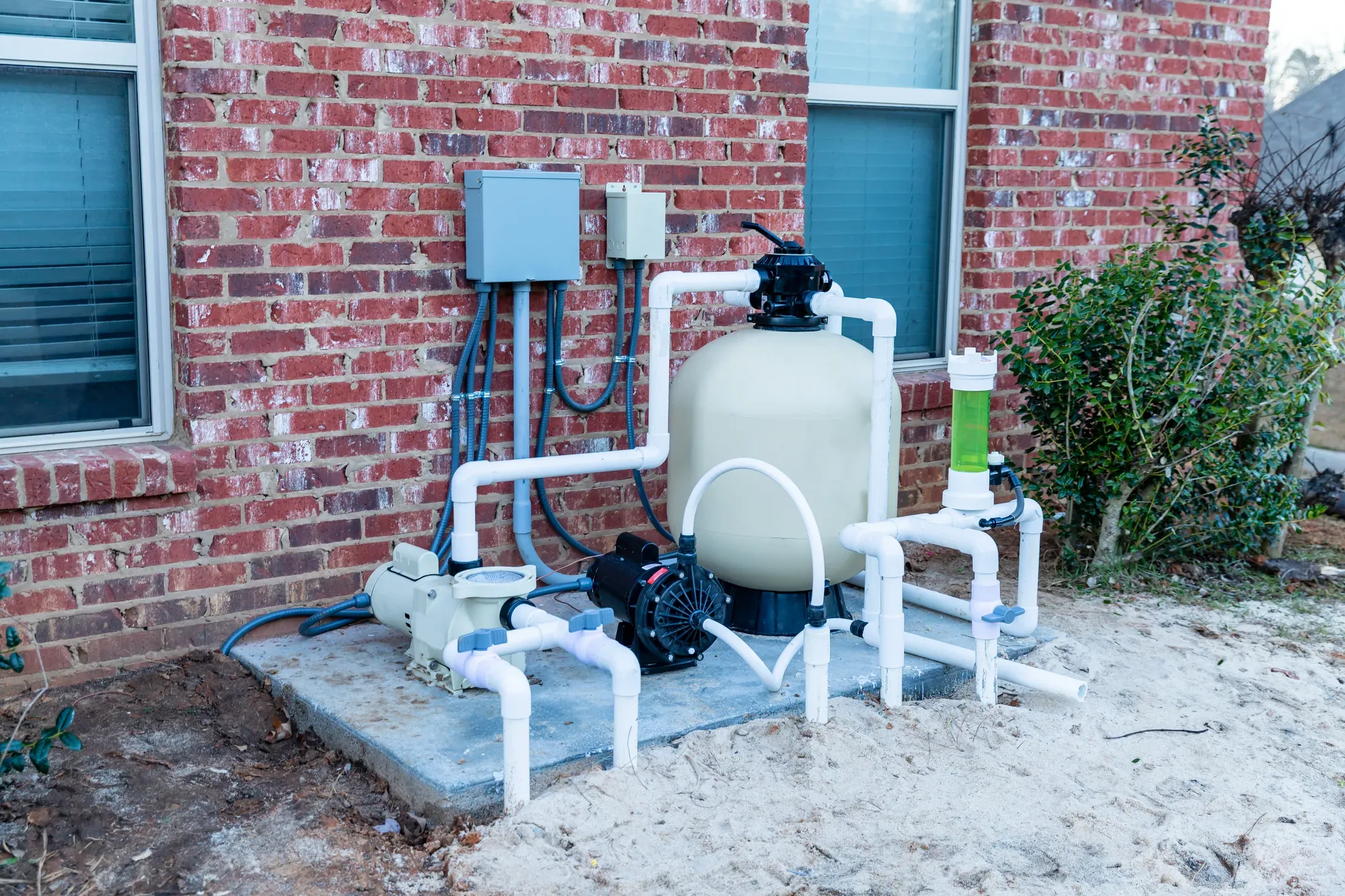 A residential pool equipment pad showing the pump, its strainer pot, a sand filter, and the PVC plumbing between them